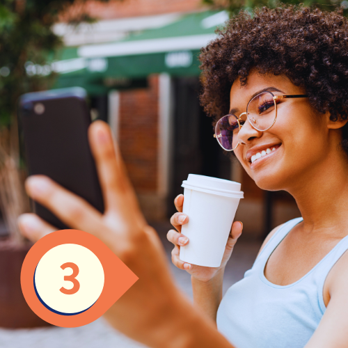 A person holding a cup of coffee and taking a selfie with their phone