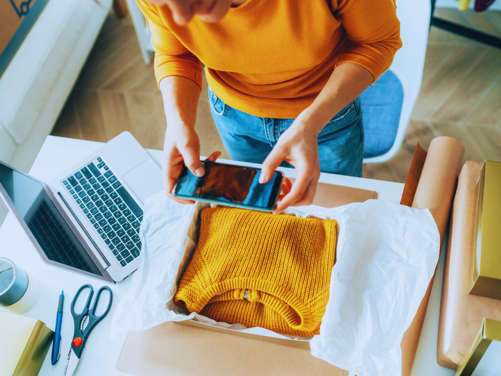 A person standing over a yellow sweater takes a photo to create social media content.